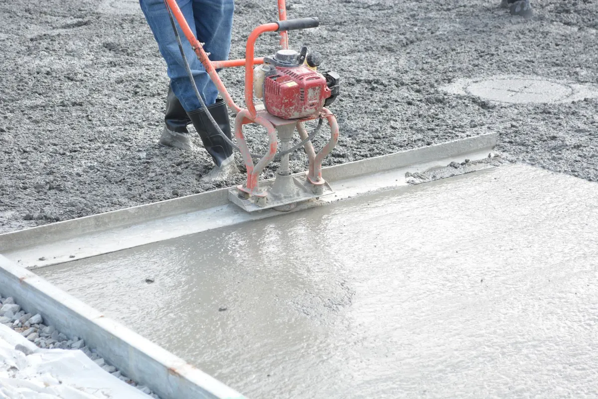 Worker leveling freshly placed concrete with a vibrating screed; illustrative stock photo