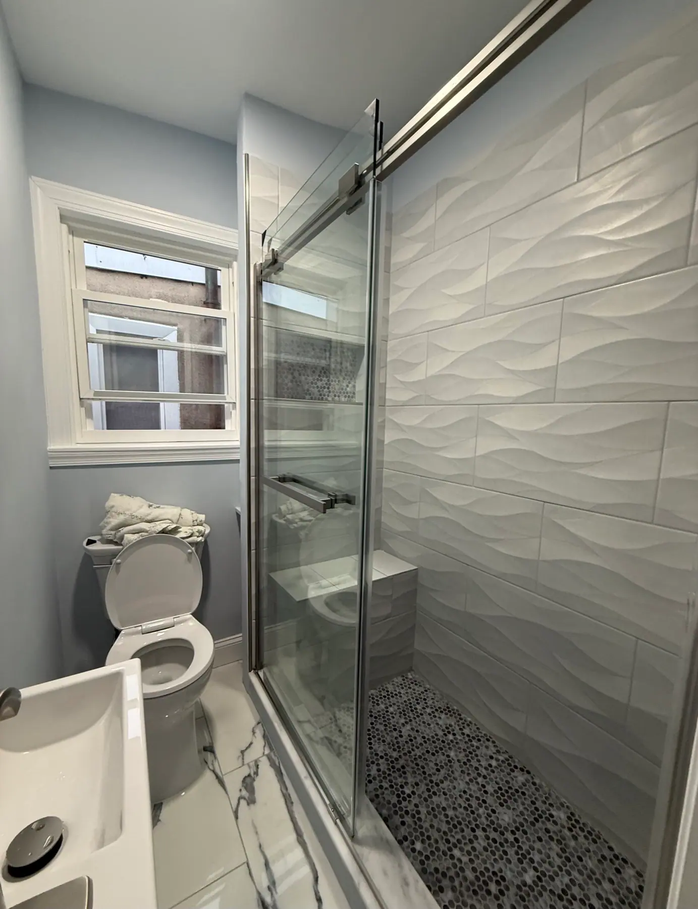 Bathroom after renovation with light tile shower wall, glass enclosure, and updated finishes